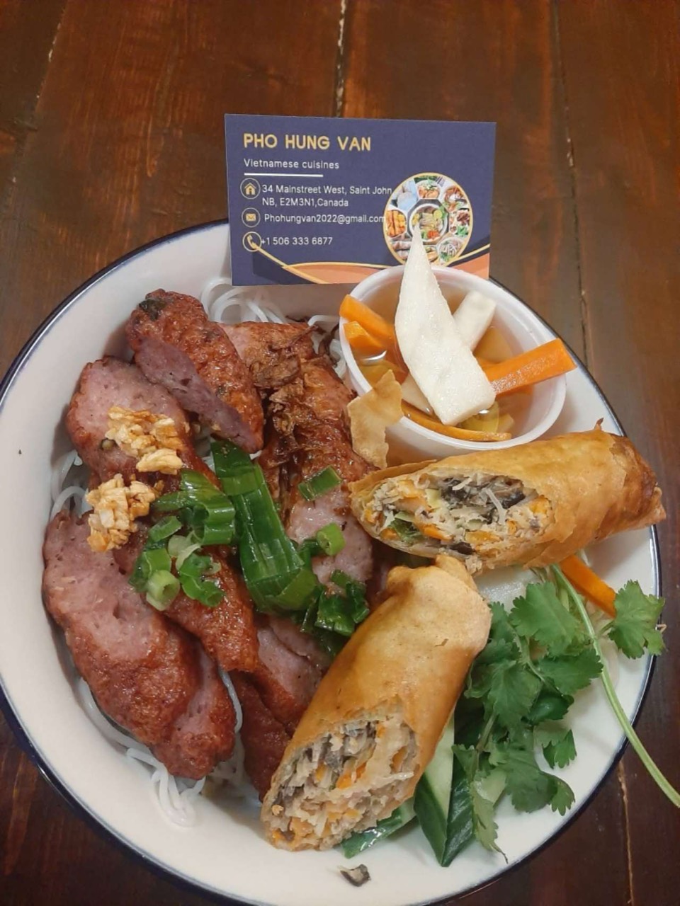 Grilled pork sausage on noodles with spring rolls and vegetables.